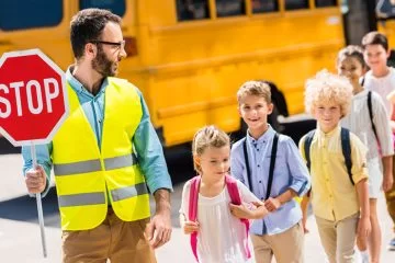 Agent en gilet de sécurité avec un panneau stop accompagnant des enfants — prévention du risque routier